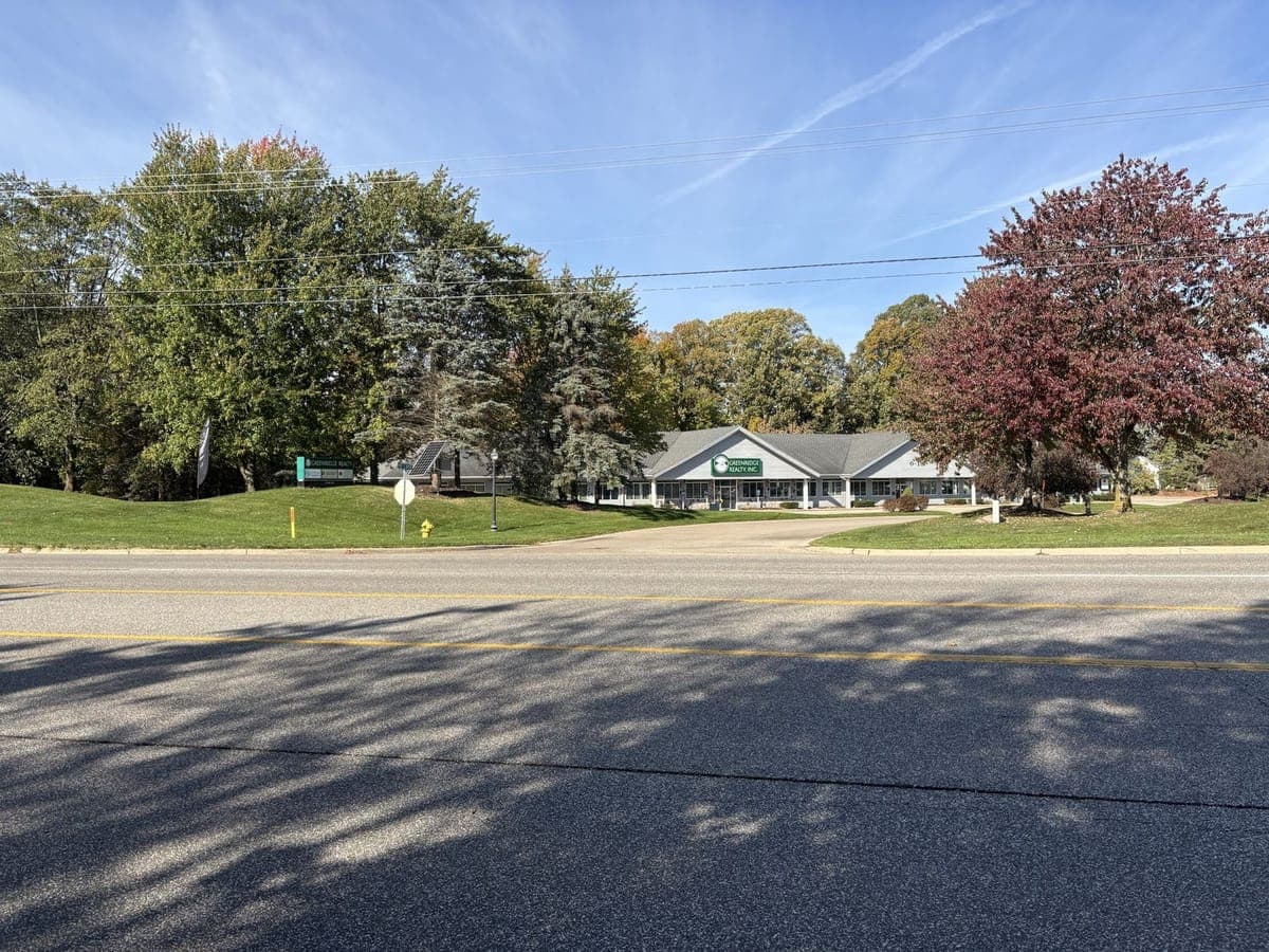 The office building seen from the road, set back behind trees, with a large green Greenridge Realty sign over the main entrance and a curved driveway.