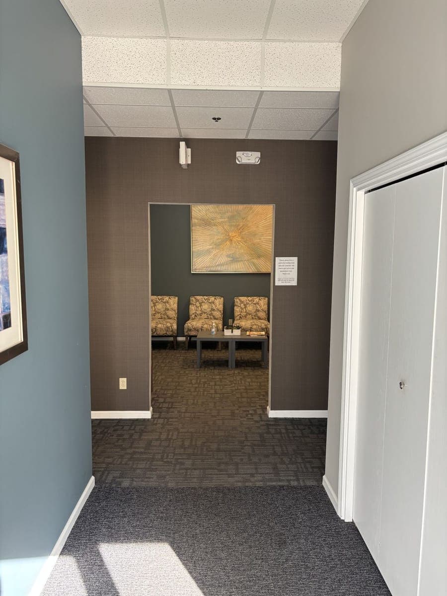 Just inside the entrance: a short hallway leading straight to the waiting room, with patterned chairs and a gold sunburst painting visible through the doorway.