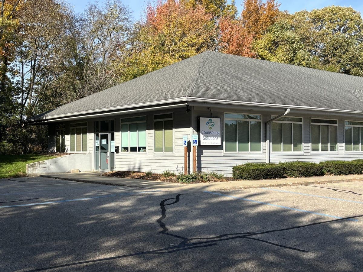 The South end of the building: a Counseling Solutions of West Michigan sign on the wall, two accessible parking signs, and the glass entrance door.